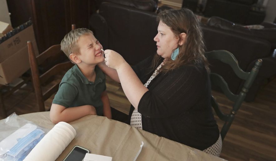 Mendy McNulty swabs the nose of her son, Andrew, 7, Tuesday, July 28, 2020, in their home in Mount Juliet, Tenn. Six thousand U.S. parents and kids are swabbing their noses twice a week to answer some of the most vexing mysteries about the coronavirus. The answers could help determine the safety of in-class education during the pandemic. (AP Photo/Mark Humphrey)