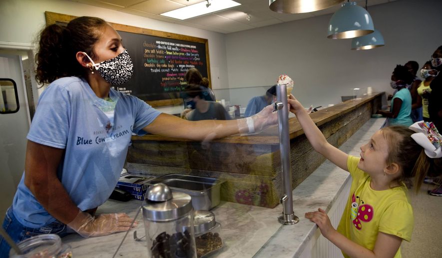 Hallie Chewing, 19, a rising junior at Liberty University serves customer, Kora Mayo, 6, a cookie dough with rainbow sprinkles cone at Blue Cow Ice Cream on July 13, 2020, in Roanoke, Va. Owner Carolyn Kiser said she’s seen an increase in job applications, although Blue Cow hasn’t needed to hire as many workers as usual. She said the ice cream shop typically employs a lot of students. (Stephanie Klein-Davis/The Roanoke Times via AP)