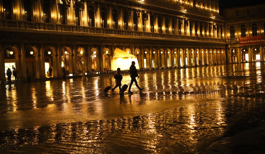 FILE - In this March 2, 2020, file photo, tourists pull their trolleys as they walk through a nearly empty St. Mark's Square on a rainy day in Venice. America's failure so far to contain the spread of the coronavirus as it moves across the country has been met with astonishment and alarm on both sides of the Atlantic. (AP Photo/Francisco Seco, File)