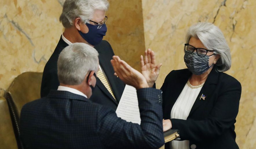House Speaker Philip Gunn, R-Clinton, back to the camera, swears into office Rep. Robin Robinson, R-Laurel, right, as her husband, former Public Service Commissioner for the Southern District Sam Britton, left, holds the Bible, Monday, Aug. 10, 2020, at the Capitol in Jackson, Miss. Robinson was elected to fulfill the unfinished term of former Republican Rep. Ramona Blackledge, also of Laurel. (AP Photo/Rogelio V. Solis)