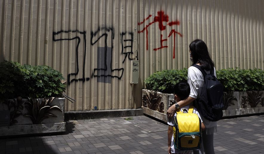 Pamela Lam and her son stand in Hong Kong, Friday, July 3, 2020. Lam's 6-year-old son fell in love with the Hong Kong protest anthem, "Glory to Hong Kong," the first time he heard it and sings it quite often. The Chinese painted on wall reads: "See you on street at July 1." Lam agreed to be photographed only if her face was not shown, fearing possible retribution from authorities. (AP Photo/Kin Cheung)