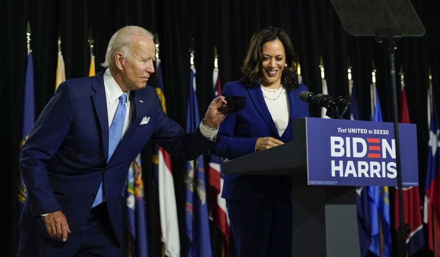 Democratic presidential candidate former Vice President Joe Biden retrieves his face mask from the podium as his running mate Sen. Kamala Harris, D-Calif., prepares to speak at a campaign event at Alexis Dupont High School in Wilmington, Del., Wednesday, Aug. 12, 2020. (AP Photo/Carolyn Kaster)