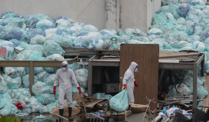Medical workers using protective equipment dispose of trash bags containing hazardous biological waste into a large pile outside the Hospital del Instituto Mexicano del Seguro Social, which treats patients with COVID-19 in Veracruz, Mexico, Wednesday, Aug. 12, 2020. Improper disposal of medical waste has become an increasing problem in Mexico amid the pandemic. (AP Photo/Felix Marquez)