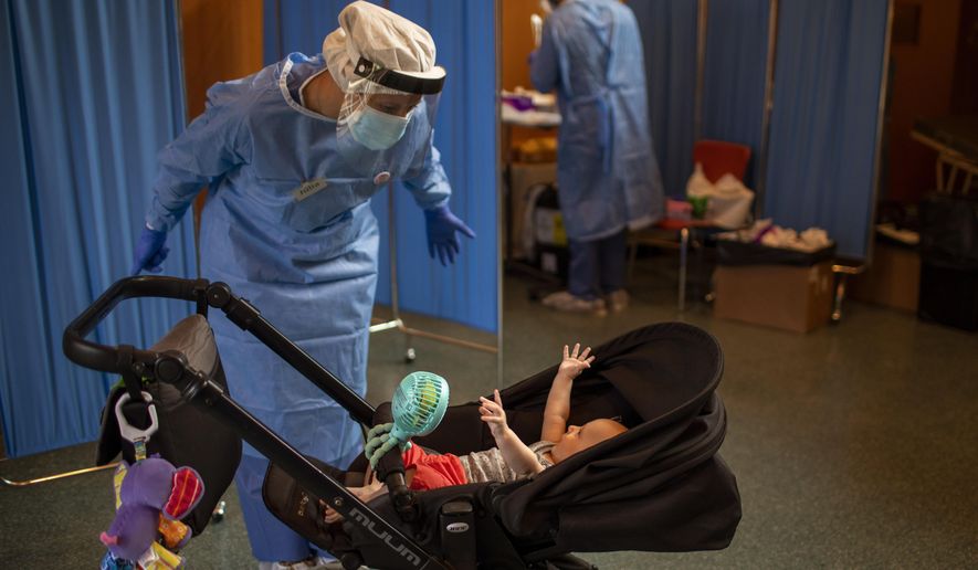 Volunteer of the Spanish NGO Open Arms Julia Martin, 38, plays with 4-month old Biel, as his father makes a PCR test for the COVID-19 coronavirus at Vilafranca del Penedes in the Barcelona province, Spain, Tuesday, Aug. 11, 2020. (AP Photo/Emilio Morenatti)