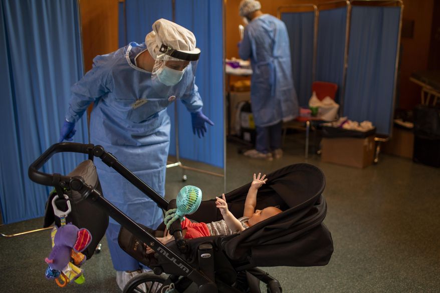 Volunteer of the Spanish NGO Open Arms Julia Martin, 38, plays with 4-month old Biel, as his father makes a PCR test for the COVID-19 coronavirus at Vilafranca del Penedes in the Barcelona province, Spain, Tuesday, Aug. 11, 2020. (AP Photo/Emilio Morenatti)