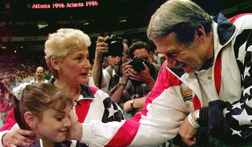 In this July 23, 1996, file photo, Bela Karolyi, right, congratulates Dominique Moceanu, left, after the United States captured the gold medal in the women&#x27;s team gymnastics competition at the Centennial Summer Olympic Games in Atlanta. United States team coach Martha Karolyi, center, looks on.(AP Photo/Amy Sancetta, File) **FILE**
