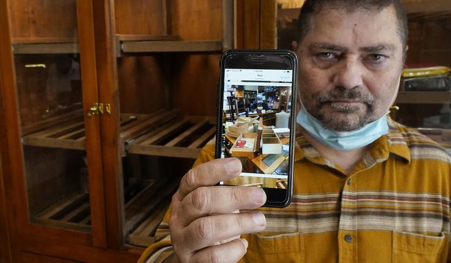 Neil Mehra, owner of the Hubbard &amp;amp; State Cigar Shop, near Chicago&#x27; Magnificent Mile, stands nears an empty humidor on Wednesday, Aug. 12, 2019, holding a cell phone image of his shop after looters stole thousands of dollars worth of merchandise and cash. “When I got here and saw what they’d done, I almost cried,” said Mehra. “This is my life. I really don’t know if we’re going to survive this.” (AP Photo/Charles Rex Arbogast)