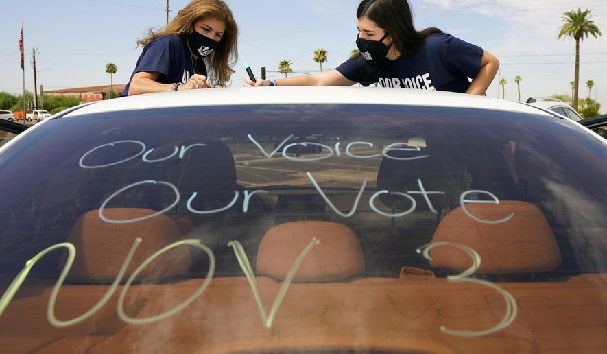 Patricia Santos, left, and her daughter Malia Santos mark their vehicle prior to a car rally Thursday, Aug. 13, 2020, at the Capitol in Phoenix. A coalition of voting rights groups in Arizona have banded together with a lofty goal of getting one million people to vote this November. (AP Photo/Matt York)