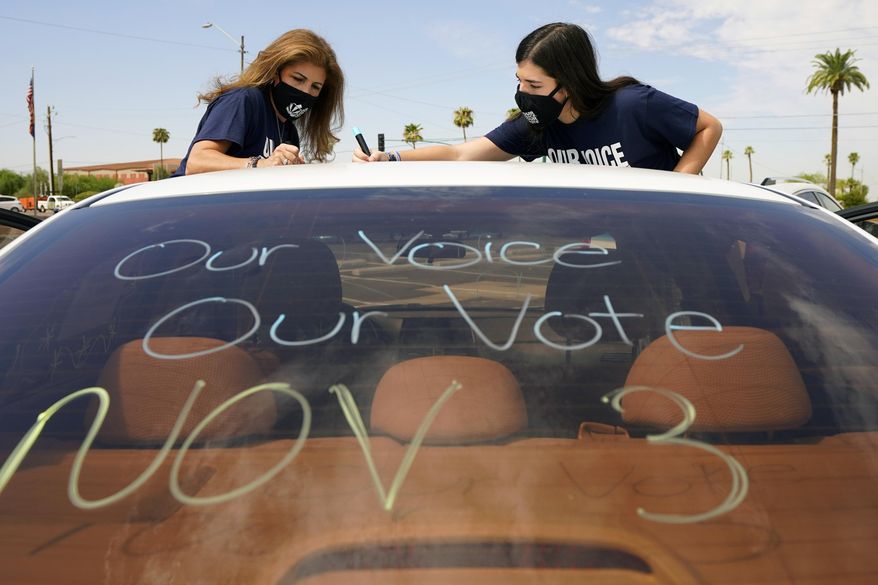 Patricia Santos, left, and her daughter Malia Santos mark their vehicle prior to a car rally Thursday, Aug. 13, 2020, at the Capitol in Phoenix. A coalition of voting rights groups in Arizona have banded together with a lofty goal of getting one million people to vote this November. (AP Photo/Matt York)