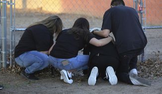 In this March 5, 2020, photo, Antonio Valenzuela&#39;s daughters, flanked by friends, kneel, at the spot their father died during an altercation with Las Cruces police on Feb. 29, 2020. An agreement announced Thursday, Aug. 13, 2020, between the city of Las Cruces and a lawyer for Valenzuela&#39;s family requires the city to provide racial bias training for police and require officers to intervene in possible excessive force episodes following Valenzuela&#39;s choking death. (Bethany Freudenthal/The Las Cruces Sun News via AP)