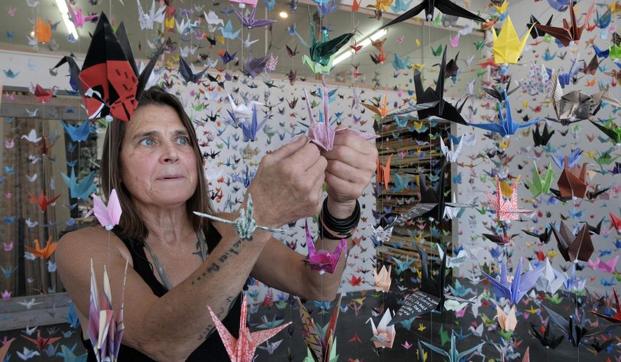 Artist Karla Funderburk, owner of Matter Studio Gallery, adjusts one of of the thousands of origami cranes hanging during an exhibit honoring the victims of COVID-19, Tuesday, Aug. 11, 2020, in Los Angeles. Funderburk started making the cranes three months earlier, stringing the paper swans in pink, blue, yellow and many other colors together and hanging them in her gallery. (AP Photo/Richard Vogel)