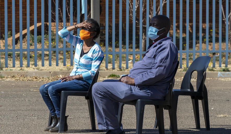 People wearing face masks to protect against coronavirus, sit on chairs whilst queuing to be screened and tested for COVID-19 in Eldorado Park outside of Johannesburg, South Africa, Monday, Aug. 3, 2020. (AP Photo/Themba Hadebe)