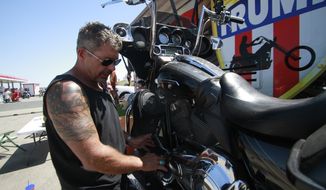 Chris Cox, the founder of Bikers for Trump, examines his motorcycle on Saturday, Aug. 8, 2020, outside the Bikers for Trump trailer he brought to the Sturgis Motorcycle Rally, in Sturgis, S.D.  The group has taken advantage of recent motorcycle rallies, which have been some of the largest mass gatherings in the country, to make direct appeals to register to vote. While the group has gained a significant online following for its shows of bravado, it remains to be seen if they can get ballot boxes filled with bikers, many who hail from the suburbs. (AP Photo/Stephen Groves)
