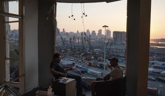 Two men sit on the destroyed balcony of a building facing the site of last week&#39;s massive explosion in the port of Beirut, Lebanon, Friday, Aug. 14, 2020. (AP Photo/Felipe Dana)