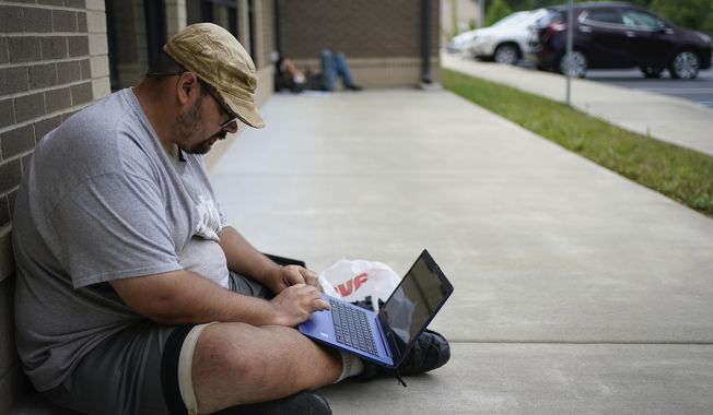Barlow Mitchell sits outside the Lee County Public Library while using the public WIFI, in Beattyville, Ky., Wednesday, July 29, 2020. As in other places, parents and officials are concerned about the virus, but dramatically limited internet access in many rural places also means kids could fall seriously behind if the pandemic keeps them home again. (AP Photo/Bryan Woolston)