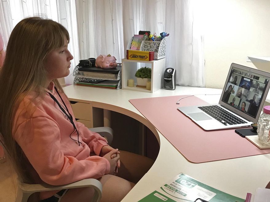 In this photo provided by Burke Burnett, Kaimuki Middle School eighth-grader Anastasiya Kamaletdinova is shown sitting in front of a computer for school in her bedroom in Honolulu on Monday, Aug. 17, 2020. Like many Hawaii public school students, she's spending the first day of school online as coronavirus cases surge, mostly on the island of Oahu, where Honolulu is located. (Burke Burnett via AP)