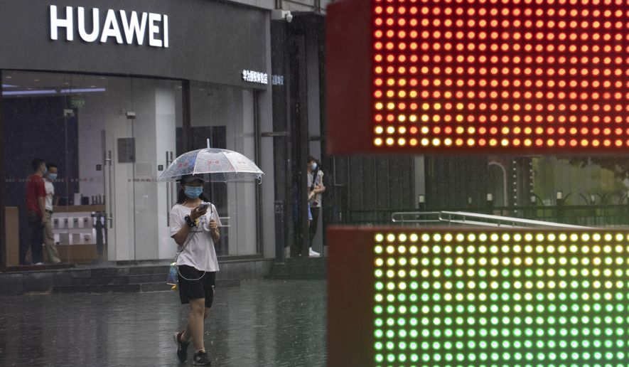 A woman wearing a mask to protect from the coronavirus walks with an umbrella as it rains outside a Huawei store in Beijing on Wednesday, Aug. 5, 2020. For nearly a decade, Huawei kept worldwide sales growing as Washington told U.S. phone companies not to buy its network equipment and lobbied allies to reject China&#39;s first global tech brand as a security threat. (AP Photo/Ng Han Guan)