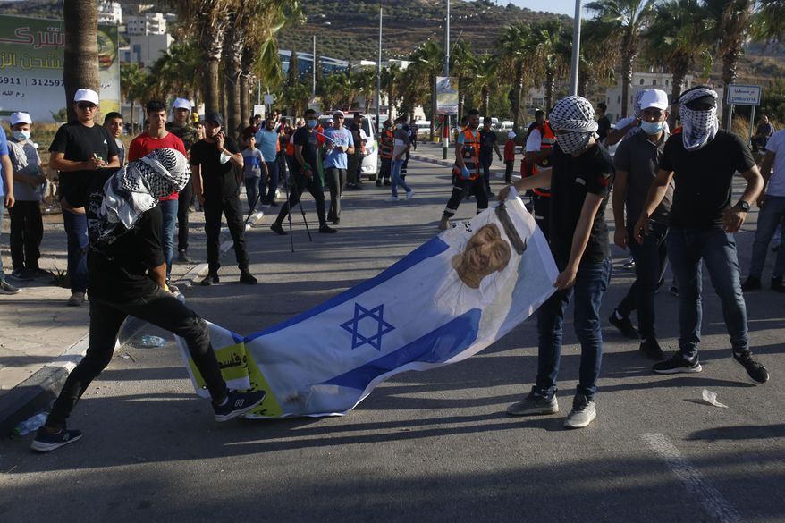 Palestinians hold a photo of Abu Dhabi Crown Prince Mohammed bin Zayed al-Nahyan wearing an Israeli flag during a rally against Israel's plan to annex parts of the West Bank and U.S. President Donald Trump's Mideast initiative as well as the United Arab Emirates' deal with Israel, in the West Bank village of Turmusaya near Ramallah, Wednesday, Aug. 19, 2020. (AP Photo/Majdi Mohammed)