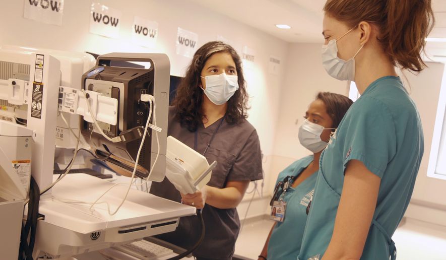 In this August 2020 photo provided by the Mount Sinai Health System, neurologist Dr. Alexandra Reynolds holds part of a device that tracks blood flow in the brain, at a hospital in New York. Reynolds was checking comatose COVID-19 patients for signs of a stroke when she stumbled onto a new clue about how the coronavirus may harm the lungs - thanks to a test that uses tiny air bubbles and a robot. (Mount Sinai Health System via AP)