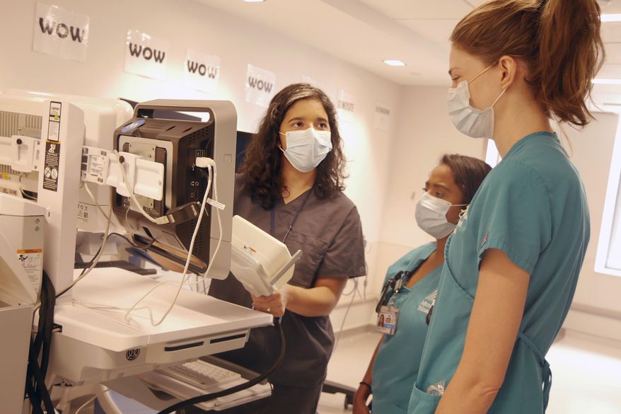 In this August 2020 photo provided by the Mount Sinai Health System, neurologist Dr. Alexandra Reynolds holds part of a device that tracks blood flow in the brain, at a hospital in New York. Reynolds was checking comatose COVID-19 patients for signs of a stroke when she stumbled onto a new clue about how the coronavirus may harm the lungs - thanks to a test that uses tiny air bubbles and a robot. (Mount Sinai Health System via AP)
