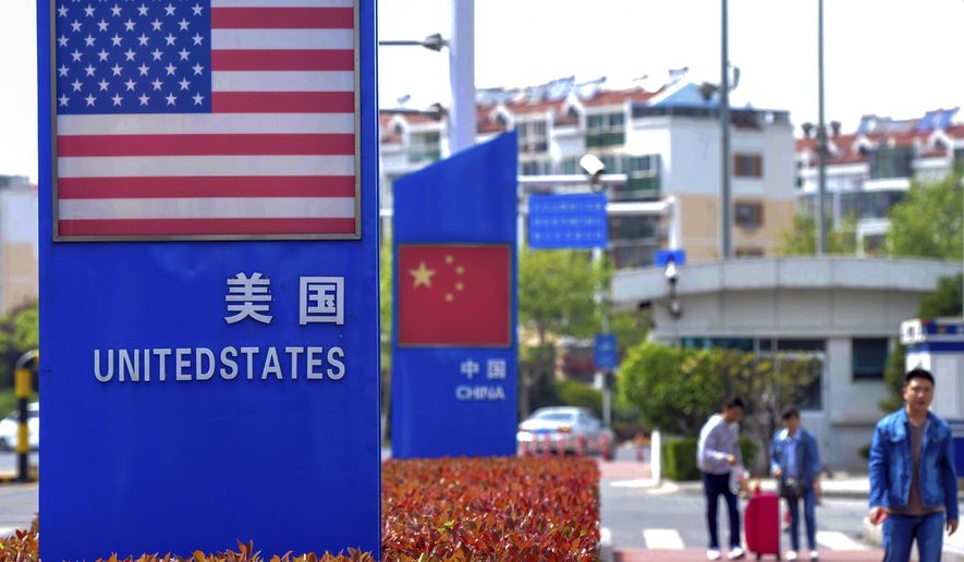 FILE - In this May 8, 2019 file photo, people walk by a display boards featuring the U.S. and Chinese flags in a special trade zone in Qingdao in eastern China's Shandong province. A Chinese Commerce Ministry official said Thursday, Aug. 20, 2020, that talks with the U.S. on a trade agreement that were postponed last week will be held "soon." (Chinatopix via AP, File)