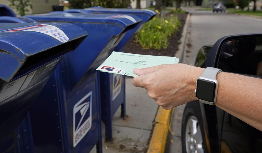 FILE - In this Tuesday, Aug. 18, 2020, file photo, a person drops applications for mail-in-ballots into a mail box in Omaha, Neb. U.S. Postal Service warnings that it can’t guarantee ballots sent by mail will arrive on time have put a spotlight on the narrow timeframes most states allow to request and return those ballots. (AP Photo/Nati Harnik, File)