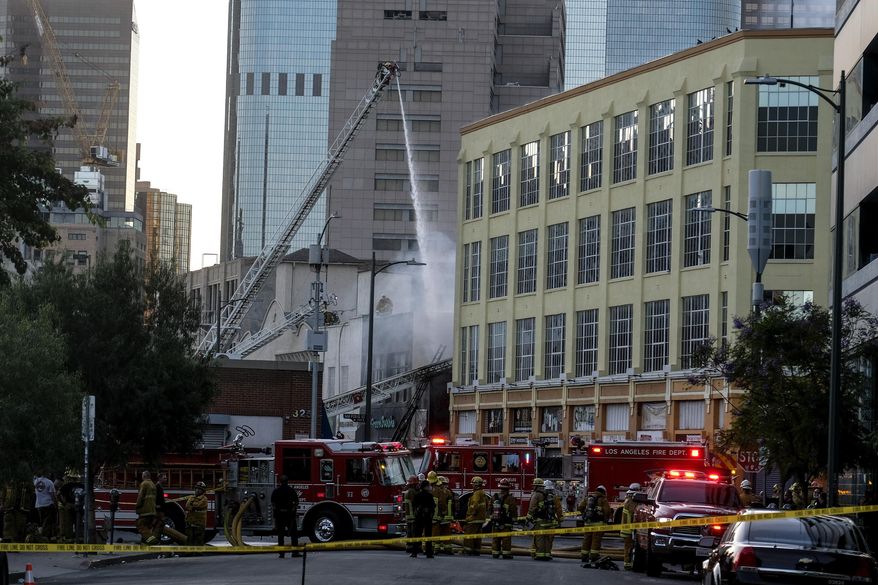 FILE - In this May 16, 2020, file photo, Los Angeles Fire Department firefighters work the scene of a structure fire that injured multiple firefighters in Los Angeles. The Los Angeles city attorney has filed dozens of criminal charges for alleged fire code and safety violations against the owner of a building that exploded in the city's downtown and injured 12 firefighters, officials announced Friday, Aug. 21, 2020. (AP Photo/Ringo H.W. Chiu, File)