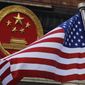 In this Nov. 9, 2017, photo, an American flag is flown next to the Chinese national emblem during a welcome ceremony for visiting U.S. President Donald Trump outside the Great Hall of the People in Beijing. (AP Photo/Andy Wong) **FILE**