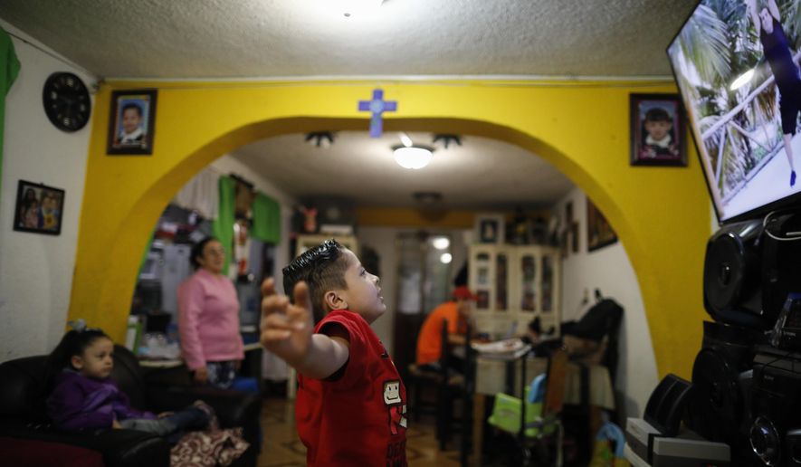 Six-year-old Santi does jumping jacks in front of a monitor during a P.E. segment of a televised kindergarten class, as his stay-at-home mother Denisse and five-year-old sister Liz look on and his father Luis works online at the dining room table, as students return to classes but not schools in Mexico City, Monday, Aug. 24, 2020. A system cobbling together online classes, instruction broadcast on cable television channels and radio programming in indigenous languages for the most remote, will attempt to keep students from missing out. (AP Photo/Rebecca Blackwell)
