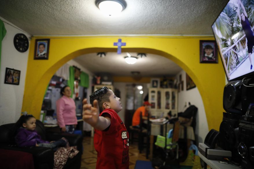 Six-year-old Santi does jumping jacks in front of a monitor during a P.E. segment of a televised kindergarten class, as his stay-at-home mother Denisse and five-year-old sister Liz look on and his father Luis works online at the dining room table, as students return to classes but not schools in Mexico City, Monday, Aug. 24, 2020. A system cobbling together online classes, instruction broadcast on cable television channels and radio programming in indigenous languages for the most remote, will attempt to keep students from missing out. (AP Photo/Rebecca Blackwell)