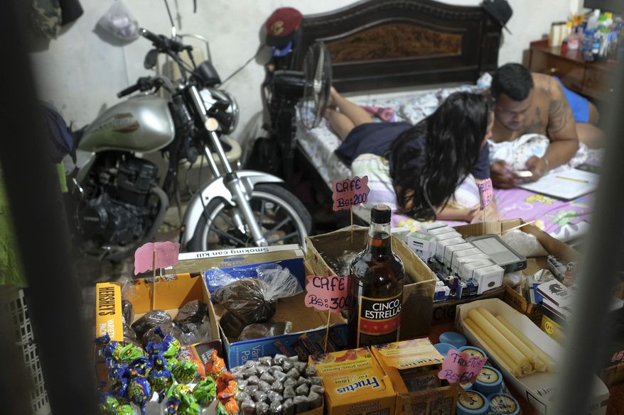 Food items, cigarettes and candles sit for sale behind the burglar bars of a private residence, where a couple calculates their sales from their bed in the Santa Rosalia neighborhood of Caracas, Venezuela, Sunday, Aug. 23, 2020. Strict measures aimed at slowing the spread of COVID-19 have left many without work, so some Venezuelans have turned their homes and other spaces into makeshift take-out restaurants or shops as they struggle to get by during the coronavirus lockdown. (AP Photo/Matias Delacroix)