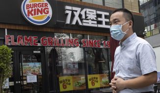 FILE - In this file photo taken Friday, July 17, 2020, a man wearing a mask to curb the spread of the coronavirus walks past a Burger King restaurant franchise in Beijing. The operator of six Burger King outlets in southern China has been required to pay more than $400,000 in fines and other penalties for using expired food, a regulator announced Tuesday, Aug 25, 2020. (AP Photo/Ng Han Guan, File)