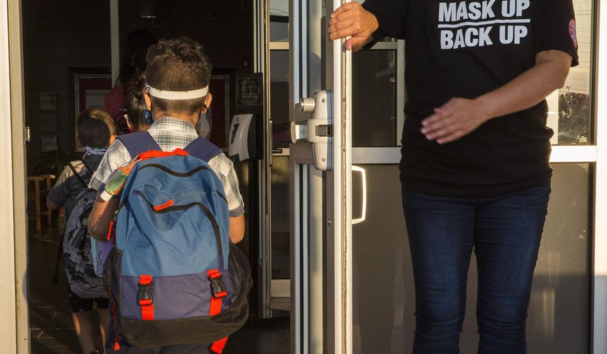 A staff member holds the door open for kids on the first day of school at Goodwin Frazier Elementary School in New Braunfels, Texas on Tuesday, Aug. 25, 2020. The number of Americans newly diagnosed with the coronavirus is falling — a development experts credit at least partly to increased wearing of masks — even as the outbreak continues to claim nearly 1,000 lives in the U.S. each day. (Mikala Compton/Herald-Zeitung via AP)