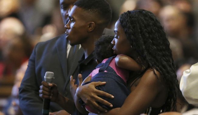 FILE - In this June 18, 2019 file photo Dravon Ames, holding microphone, speaks to Phoenix Police Chief Jeri Williams and Phoenix Mayor Kate Gallego, as his fiancee, Iesha Harper, right, holds 1-year-old daughter London, at a community meeting, in Phoenix. The Phoenix City Council will vote Wednesday, Aug. 26, 2020 on a settlement for the Black couple who had police officers point guns at them in front of their children last year after their young daughter took a doll from a store without their knowledge. (AP Photo/Ross D. Franklin, File)