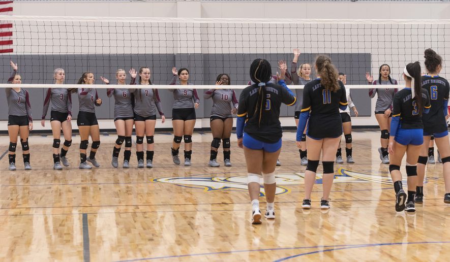 Arp High School's varsity volleyball team approaches the net from a safe distance to wave to the Cumberland Academy team in lieu of shaking hands at the start of a match at Cumberland Academy on Tuesday, Aug. 25, 2020, in Tyler, Texas. (Sarah A. Miller/Tyler Morning Telegraph via AP)
