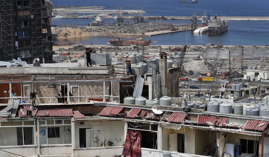 Workers repair water tanks and damaged apartments overlooking the site of the Aug. 4 explosion that hit the seaport, in Beirut, Lebanon, Thursday, Aug. 27, 2020. (AP Photo/Hussein Malla)
