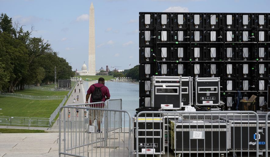 With the Washington Monument in the background, people walk by equipment being set up near the reflection pool on Thursday Aug. 27, 2020, in Washington, prior to the March on Washington, which is being held on Friday at the Lincoln Memorial. (AP Photo/Jacquelyn Martin)