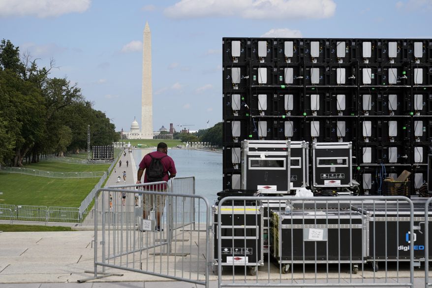 With the Washington Monument in the background, people walk by equipment being set up near the reflection pool on Thursday Aug. 27, 2020, in Washington, prior to the March on Washington, which is being held on Friday at the Lincoln Memorial. (AP Photo/Jacquelyn Martin)