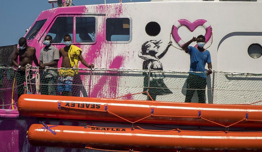 A boy waves to the crew of the Astral rescue vessel from the deck of the Louise Michel rescue vessel, a French patrol boat currently manned by activists and funded by the renowned artist Banksy in the Central Mediterranean sea, at 50 miles south from Lampedusa, Friday, Aug. 28, 2020. A Berlin-based group says it has begun migrant rescue operations in the Mediterranean Sea with a bright pink former navy vessel sponsored by British artist Banksy. The group operating the MV Louise Michel, a sleek 30-meter (98-foot) ship named after a 19th century French feminist and anarchist, said late Thursday that it rescued 89 from an inflatable boat in distress. (AP Photo/Santi Palacios)