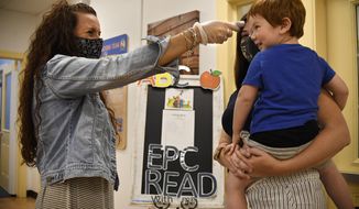 In this Thursday Aug. 27, 2020 photo, Assistant Director Tammy Cavanaugh, left, takes the temperature of Maverick Barbera has he is held by his mother Katrina Meli at Educational Playcare, in Glastonbury, Conn. All children entering the daycare have their temperature taken. (AP Photo/Jessica Hill)