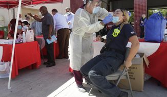 FILE - In this Aug. 6, 2020, file photo, Hialeah Fire Department Firefighter-Paramedic Laura Nemoga, right, winces as medical assistant Jesus Vera performs a COVID-19 test at Hialeah Fire Station #1, in Hialeah, Fla. The torrid coronavirus summer across the Sun Belt is easing after two disastrous months that brought more than 35,000 deaths. (AP Photo/Wilfredo Lee, File)
