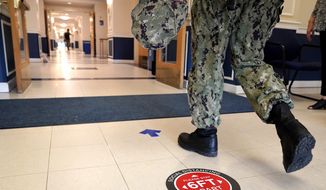 A social distancing sign is seen on the floor as a midshipman walks to class at Luce Hall at the U.S. Naval Academy, Monday, Aug. 24, 2020, in Annapolis, Md. Under the siege of the coronavirus pandemic, classes have begun at the Naval Academy, the Air Force Academy and the U.S. Military Academy at West Point. But unlike at many colleges around the country, most students are on campus and many will attend classes in person. (AP Photo/Julio Cortez)