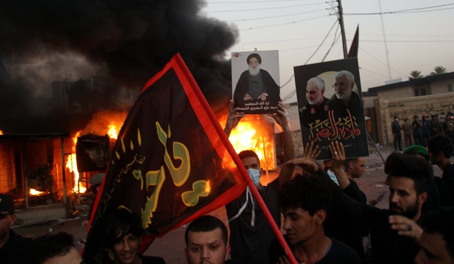 Supporters of an Iran-backed militia hold posters of Iranian General Qassem Soleimani, deputy commander Abu Mahdi al-Muhandis and Grand Ayatollah Ali al-Sistani, center, while burning the building of Dijala local TV channel accusing it of broadcasting songs and dance on the holy Shiite day of Ashoura in Baghdad, Iraq, Monday, Aug. 31, 2020. (AP Photo/Khalid Mohammed)