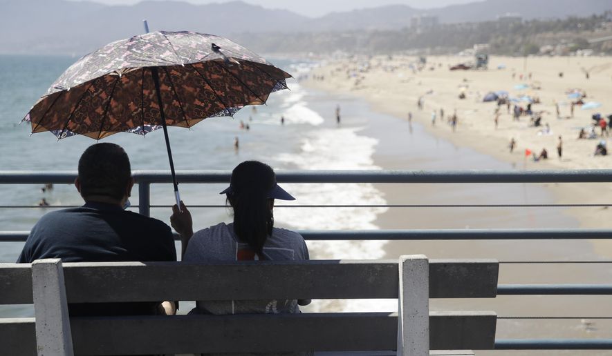 FILE - In this July 12, 2020, file photo, visitors sit on a bench on the pier amid the coronavirus pandemic in Santa Monica, Calif. California will roast in a dangerous heat wave through the Labor Day weekend and options for cooling off may be limited by coronavirus concerns at beaches and calls for energy conservation that could limit use of air conditioning at home. (AP Photo/Marcio Jose Sanchez, File)