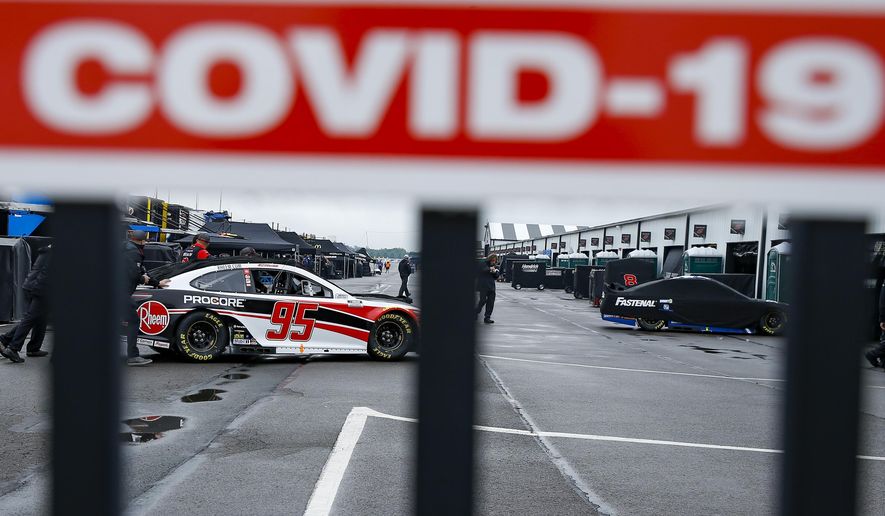 FILE - Crew members are visible under a COVID-19 alert sign as they push the car of Christopher Bell through the garage area before a scheduled NASCAR Cup Series auto race at Pocono Raceway, Saturday, June 27, 2020, in Long Pond, Pa. NASCAR will not grant COVID-19 relief during the playoffs which means a positive coronavirus test will end a drivers&#x27; championship bid. (AP Photo/Matt Slocum, File)