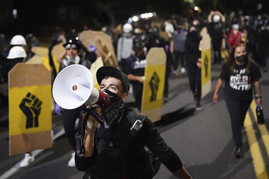 In this Aug. 7, 2020, file photo, a protester leads a crowd of demonstrators toward the Multnomah County Sheriff's Office in Portland, Ore. Reporters — whether they're from major media outlets, freelancers or self-proclaimed “citizen journalists" — say they are doing their job and law enforcement is hindering that work. Police say protesters have masqueraded as journalists and then set fires or thrown fireworks, making it a struggle to figure out who is a real reporter during the pandemonium. (AP Photo/Nathan Howard, File) **FILE**