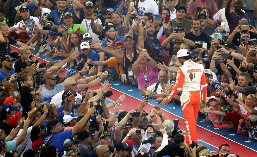 FILE - Fans reach out to high-five pole-sitter Chase Elliott during driver introductions for the NASCAR Sprint Cup auto race at Daytona International Speedway, Saturday, July 7, 2018, in Daytona Beach, Fla. NASCAR has built itself around its traveling show, every weekend a super-charged event of concerts, camping and infield carousing that closes with a Cup race. The party has been canceled during the pandemic but the playoffs go on, starting Sunday, Sept. 6, 2020, without any of the pomp and circumstance. (AP Photo/John Raoux, File)