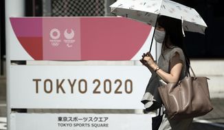 A woman wearing a face mask to help curb the spread of the coronavirus walks in front of Tokyo 2020 sign Friday, Sept. 4, 2020, in Tokyo. The CEO of the Tokyo Olympics Toshiro Mut said Friday that having a vaccine is not a requirement for holding next year Olympics and Paralympics. (AP Photo/Eugene Hoshiko)