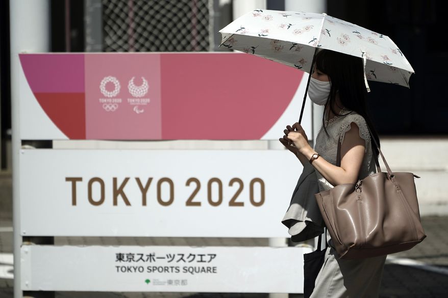A woman wearing a face mask to help curb the spread of the coronavirus walks in front of Tokyo 2020 sign Friday, Sept. 4, 2020, in Tokyo. The CEO of the Tokyo Olympics Toshiro Mut said Friday that having a vaccine is not a requirement for holding next year Olympics and Paralympics. (AP Photo/Eugene Hoshiko)