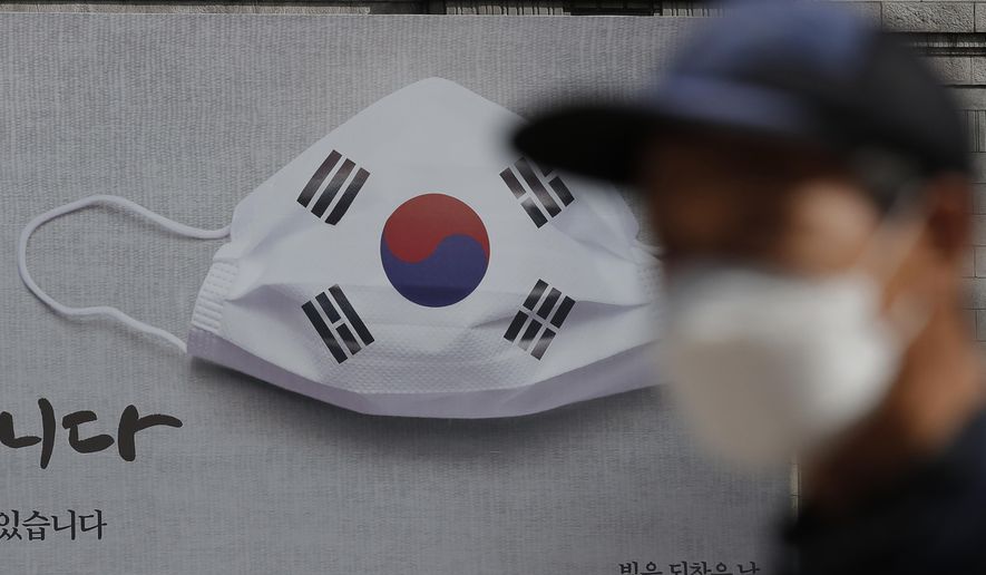 A man wearing a face mask walks near a banner displaying as a part of campaign to overcome the coronavirus in Seoul, South Korea, Friday, Sept. 4, 2020. (AP Photo/Lee Jin-man)